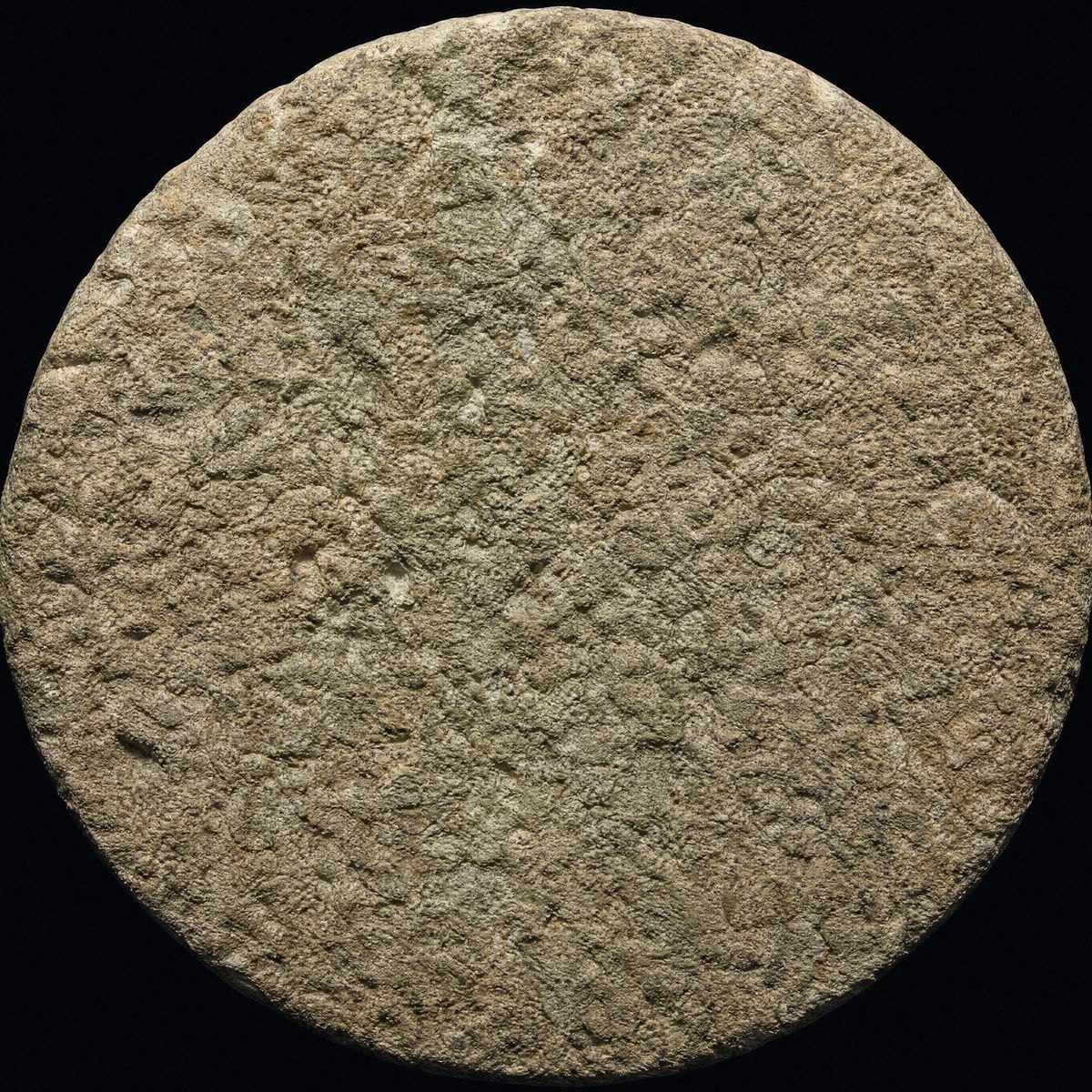 A great circular hewn stone — a first-century rolling tomb stone — seen straight on against darkness.