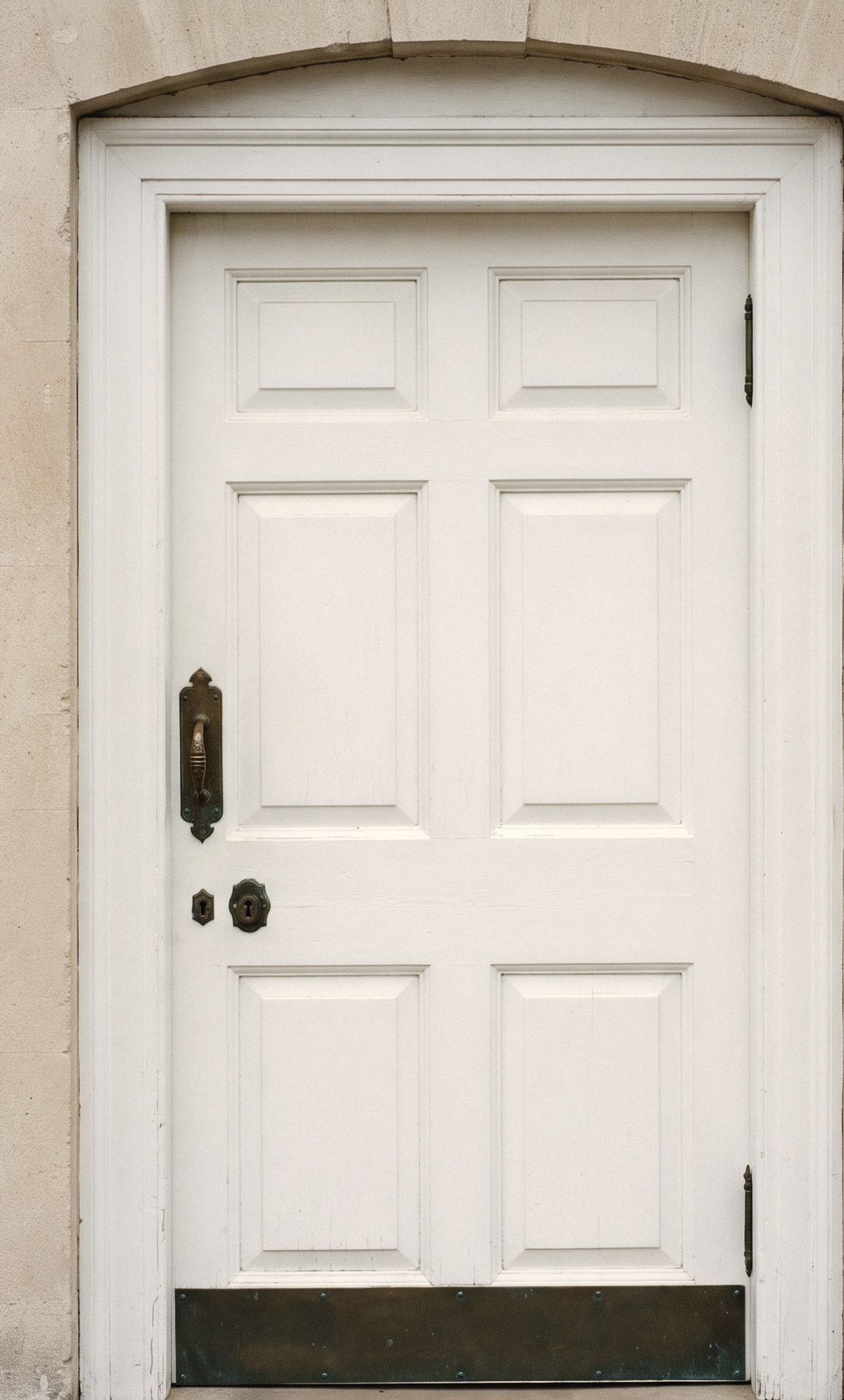 A white painted paneled church door with aged brass hardware, photographed straight on.